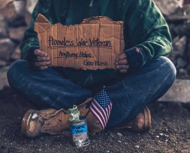 A homeless veteran holding a sign reading 'Homeless War Veteran — Anything Helps'